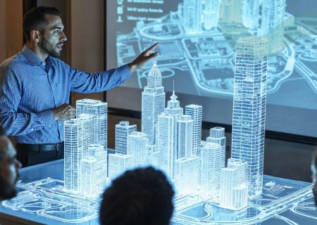 A man gestures toward a 3D illuminated architectural model of a cityscape on a table, appearing engaged and focused. A projected city map is in the background.