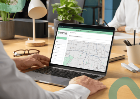 A person at a desk uses a laptop displaying a map on the screen in an office setting. Nearby, glasses and a small plant create a focused, modern atmosphere.